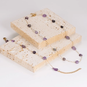 Elegant gold chain necklace with purple gemstones and white beads on stone surface