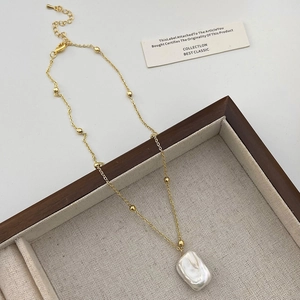 Detail shot of a rectangular baroque pearl pendant on a gold beaded chain necklace
