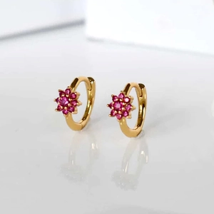 Macro shot of gold huggie hoop earrings featuring pink zircon flower design details