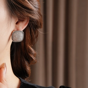 Detail view of square pavé stud earrings with sparkling zircons on a model's ear