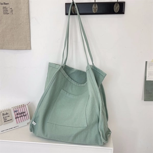 Detail of light grass green canvas tote bag featuring a large front pocket and strap