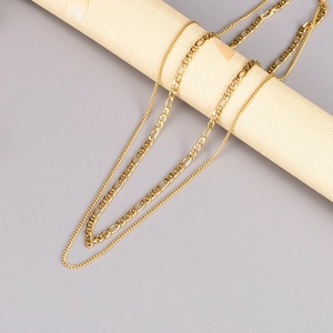 Layered gold Figaro and slim chain necklace set displayed on a textured pedestal