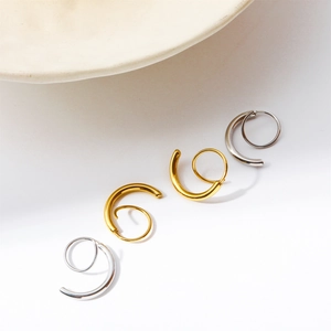 Detail shot of spiral double twist hoop earrings in gold and silver finish on ceramic
