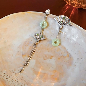 Asymmetric fan-shaped earrings with light green jade and tassels on a ceramic plate