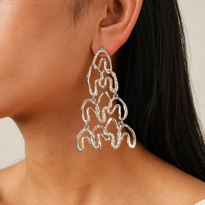 Detailed view of large silver wave earrings with sparkling diamond accents on model