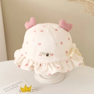Close-up of white baby bucket hat with pink heart patterns and ruffle brim detail