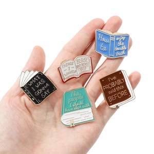 Set of five colorful book-shaped enamel pins featuring witty literary quotes on a hand