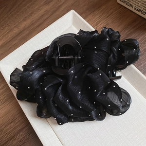 Detail of a large black mesh hair claw clip with rhinestones on a wooden surface