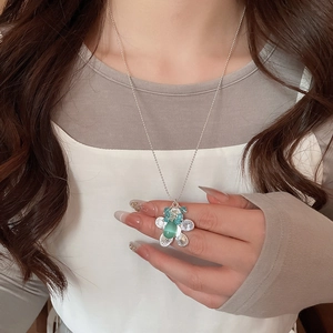 Close-up of floral silver necklace with green gemstone worn on model's neck