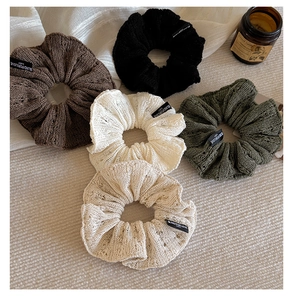 Flat lay of five knitted scrunchies in neutral tones on a textured fabric background