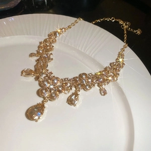 Macro shot of gold floral drop necklace with champagne pear-cut crystals on white ceramic