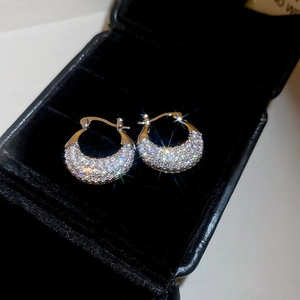 Close-up of gold U-shaped earrings with zircon crystals in a black velvet box