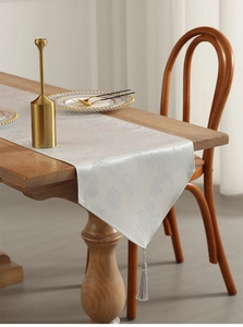 Detail of silver gray jacquard table runner with fringe tassels on a wooden dining table