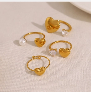 Close-up of four gold heart rings featuring pearls and zircon on linen background