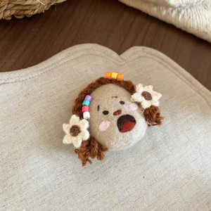 Close-up of handmade wool felt girl brooch with colorful beads on a linen background
