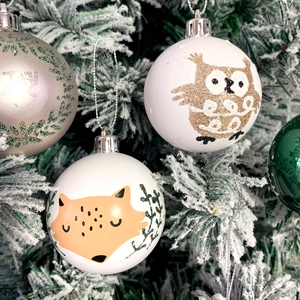 Detail of Christmas tree baubles with fox and owl motifs on white flocked branches