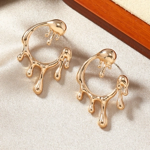 Macro detail of golden lava liquid fluid earrings resting on minimalist textured fabric