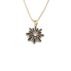 Close-up of golden chain necklace featuring a black daisy pendant with a clear center gem
