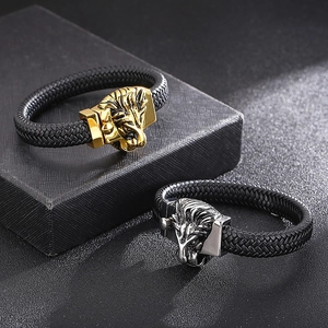 Détail de breloques tête de lion sur des bracelets en cuir tressé doré et argenté