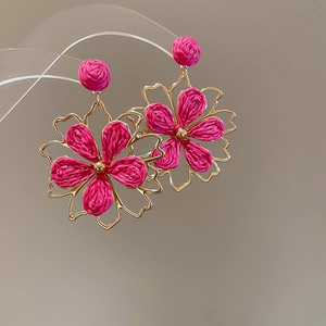 Detail of fuchsia woven flower earrings with gold metal frame and hanging texture