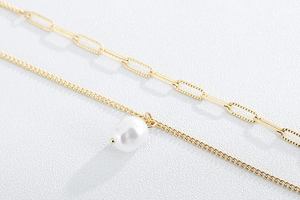 Detail of gold paperclip chain and baroque pearl pendant on layered necklace