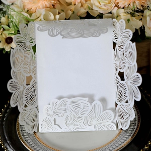 Detailed laser-cut white wedding invitation with intricate floral patterns on a dark plate