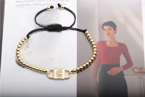 Detail of adjustable black woven bracelet with golden beads and a rhinestone C pendant