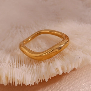 Macro view of gold irregular wavy ring displayed on white coral over pink fabric