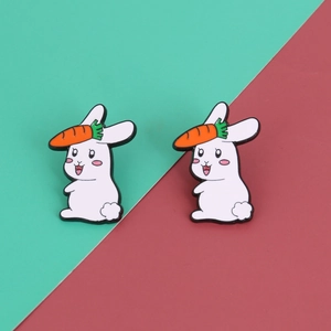 Detail of two white rabbit enamel pins with orange carrots on green and red background