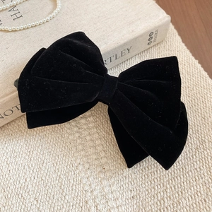 Close-up of black velvet bow hair clip with matte texture on vintage beige linen