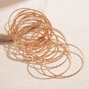 Dettaglio di 20 bracciali sovrapposti in metallo dorato con superficie sfaccettata