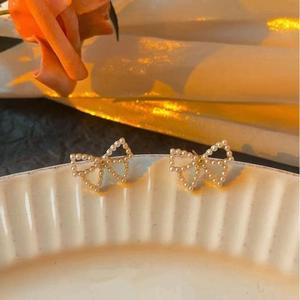 Detail of bow-shaped pearl stud earrings on ceramic tray with orange rose decoration