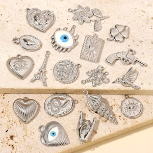 Selection of diverse stainless steel charms including hummingbird and heart on stone surface