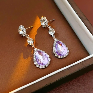 Detail of luxury silver teardrop earrings with purple gemstones in a jewelry box