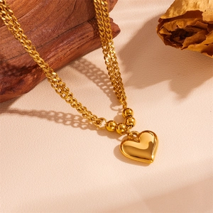 Collana a doppio strato con pendente a cuore dorato e perle su sfondo testurizzato