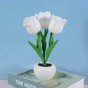 Close-up of white LED tulip lamp in a ceramic pot on a book with a light blue background