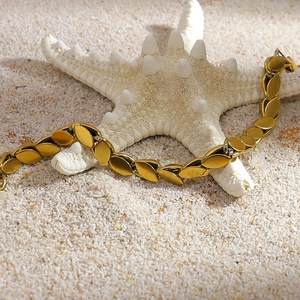 Close-up of 18K gold plated leaf link bracelet on beach sand with a white starfish