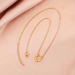 Detail of gold U-shaped pendant necklace with lobster clasp on pink silk background