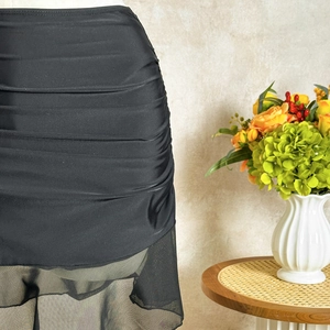 Detail of ruched black skirt with mesh hem on a mannequin in a cozy home setting