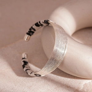 Detail of silver twisted metal bracelet with zebra print resin ends on ceramic stand