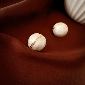Detailed close-up of pearl white stud earrings with gold chain link wrap on silk fabric