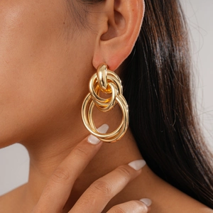 Close-up of model wearing chunky layered geometric gold knot hoop earrings