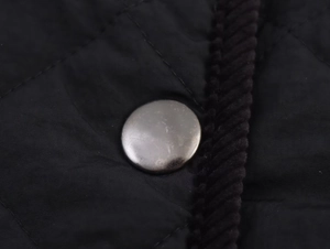 Macro detail of black quilted nylon fabric with metal button and corduroy piping edge