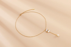 Detail of golden LOVE necklace with shell disc, pearl drop and lobster clasp fastener