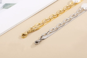 Detail of layered gold and silver snake chains with white heart pendant on beige background