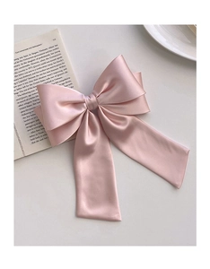 Detail of a large pink satin bow hair clip placed on an open book for a French romantic aesthetic