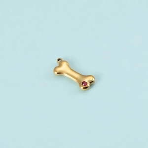Detailed view of a gold bone pendant featuring a vibrant red zircon stone on blue background