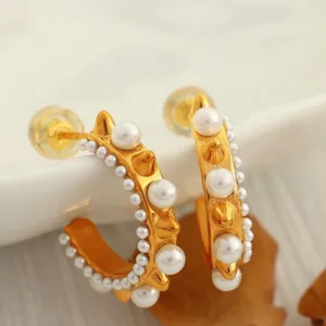 18K gold-plated hoop earrings with large pearls and metallic spikes on ceramic surface