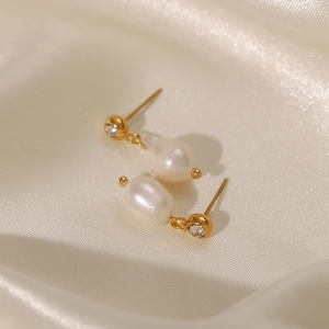 Detalle macro de pendientes de aro con perlas bañados en oro de 18K y circón sobre seda
