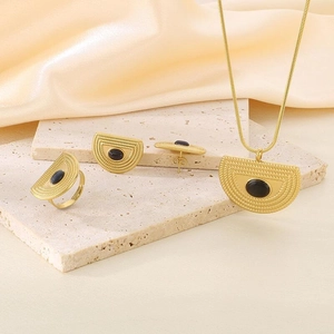 Set gioielli in titanio dorato con pietre ovali nere su sfondo elegante in seta